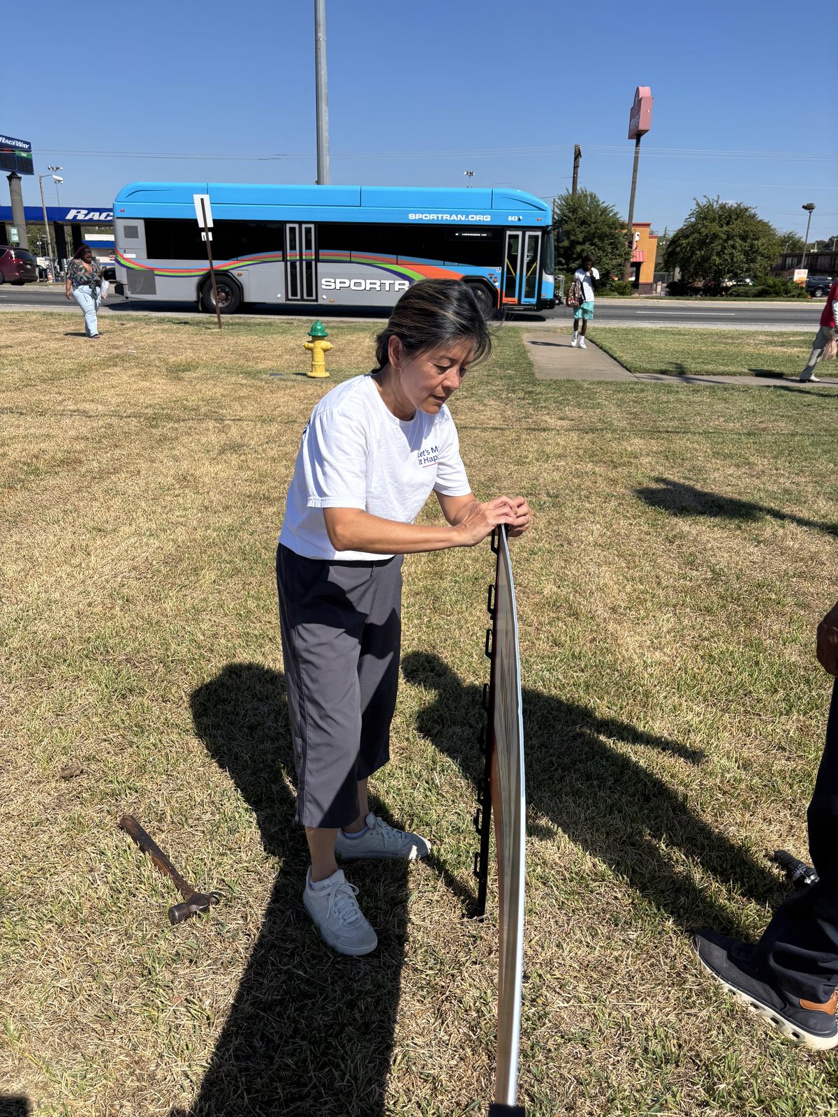 Hanh Williams setting a campaign sign frame into the grass beside a Shreveport street, October 7, 2026